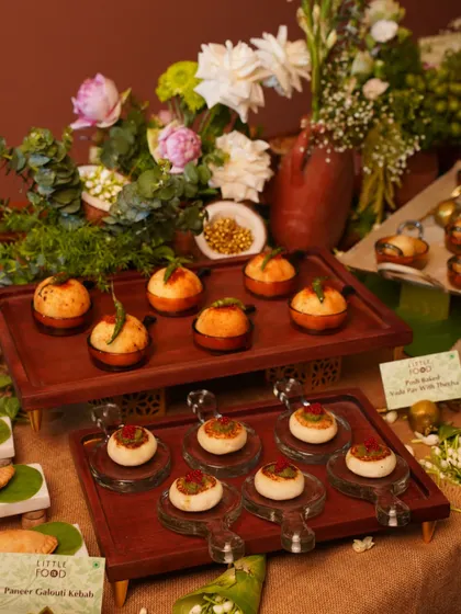 A tiered display of our Pot-Baked Vada Pav with Chutney and Paneer Galouti Kebabs. This setup, adorned with fresh flowers, showcases our innovative take on traditional Indian street food.