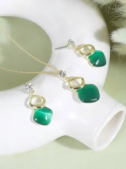 A minimalist shot of a necklace and earring set with green stones. The white prop and background keep the focus on the jewelry's color and elegant design.