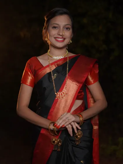 A direct and engaging portrait for Makar Sankrant. The subject looks straight at the camera with a warm smile, showcasing her traditional black saree and gold jewelry against a softly lit background.