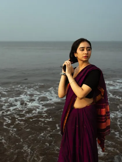 The movement of the saree in the water creates a beautiful, flowing texture in this beach portrait.