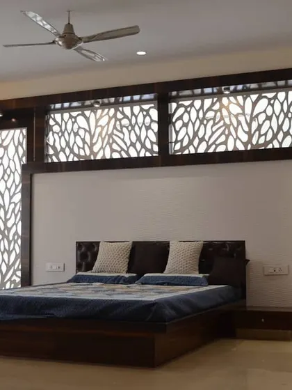 This spacious master bedroom features an elaborate custom headboard wall with integrated, backlit jaali panels in a nature-inspired pattern. The dark wood finish and clean lines of the bed frame create a look of contemporary elegance.