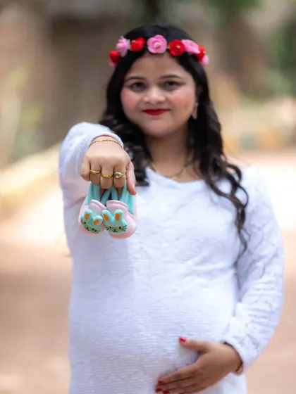 A sweet close-up of a mom-to-be holding a pair of tiny bunny shoes towards the camera.