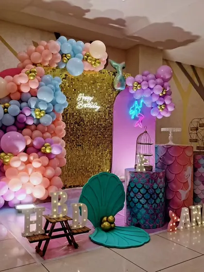 A side view of a mermaid-themed sixth birthday, showing the shimmering gold backdrop and pastel balloon arch.