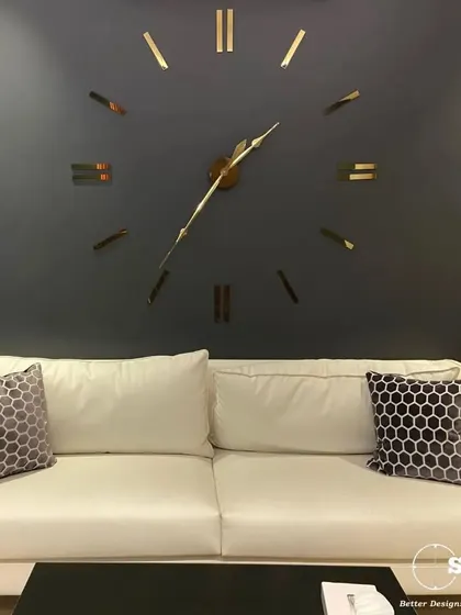 This lounge area features a large, minimalist wall clock as a focal point above a contemporary white sofa. The dark accent wall and honeycomb-patterned cushions add depth and texture to the space.