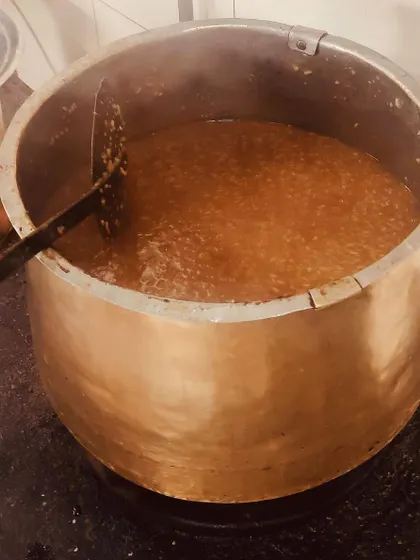 Sakkarai Pongal, a sweet rice dish made with jaggery, being slow-cooked in a large brass vessel. This traditional method ensures even cooking and a richer taste.