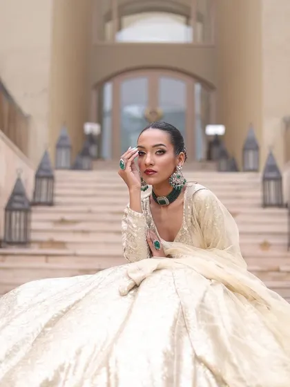 An elegant bride in an ivory lehenga. The makeup is classic, with a bold red lip and winged liner.