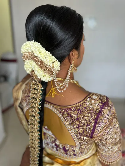 A three-quarter view of a traditional bridal hairstyle, highlighting the neatness of the bun and the flow of the `jadai`.