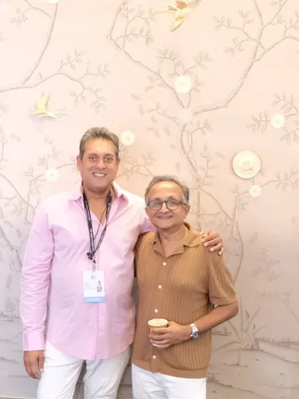A guest poses in front of a delicate Chinoiserie wallpaper at our ID Mumbai booth. The design features finely drawn branches with small birds and circular inlays, showcasing a modern take on a classic style.
