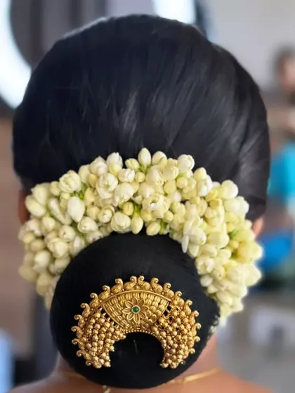 A perfectly neat low bun adorned with a crescent-shaped gold accessory and a full jasmine gajra.