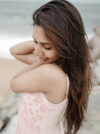 A candid and gentle portrait taken at the beach. Her soft smile and the way she adjusts her hair feel completely natural, capturing a quiet moment of self-reflection.