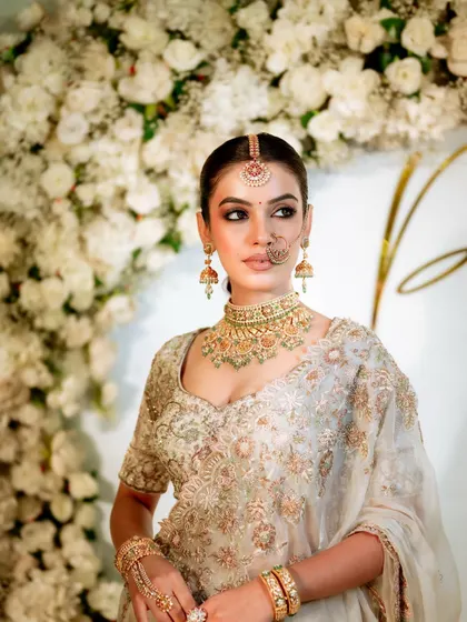A striking portrait against a wall of white flowers. The bride's makeup, with its defined eyes and flawless skin, stands out beautifully.