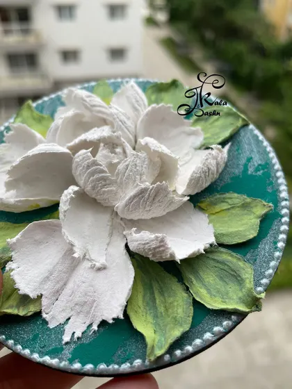 A close-up of the beautiful white flower on the green fridge magnet, showing the delicate texture of each petal.