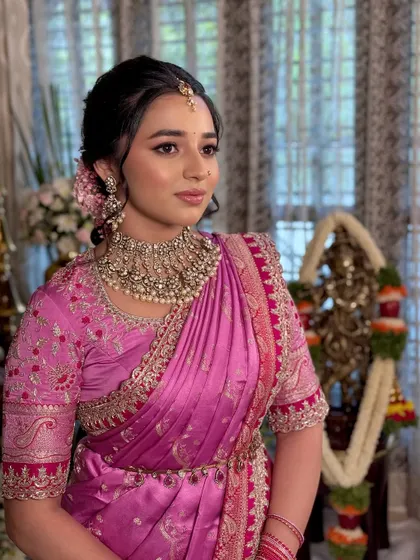 A side view showing the elegant hairstyle, adorned with fresh pink flowers to match her saree, and the soft, dewy makeup.