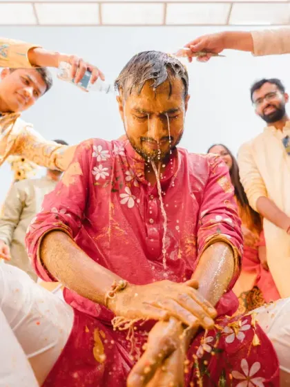 The groom gets a refreshing (or shocking!) dousing of water from his friends. This action shot captures the peak of the haldi fun and games.