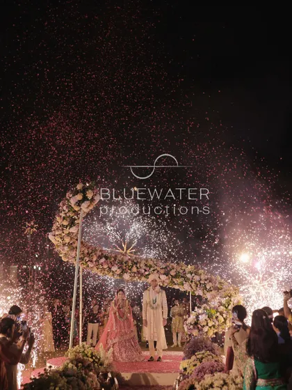 A magical Varmala moment, with the couple showered in confetti and framed by a floral arch and cold pyros.