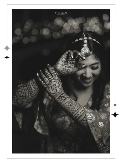 A classic black and white portrait of the bride admiring her mehendi. This timeless shot highlights the intricate patterns and her happy, gentle expression against a backdrop of festive lights.