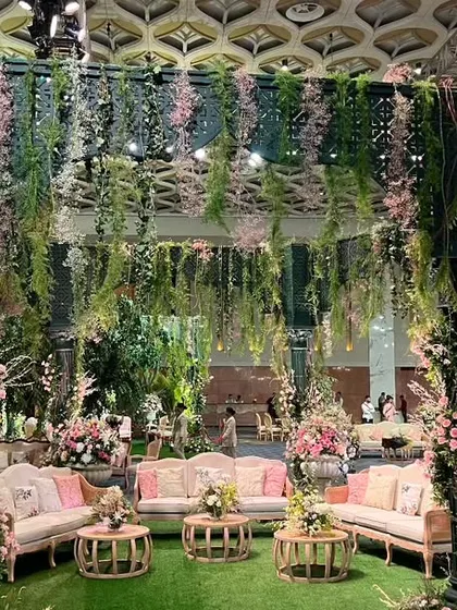 A lounge area set within the Italian garden theme, featuring a canopy of hanging vines and flowers. The pastel pink seating adds a soft, romantic touch to the green surroundings.