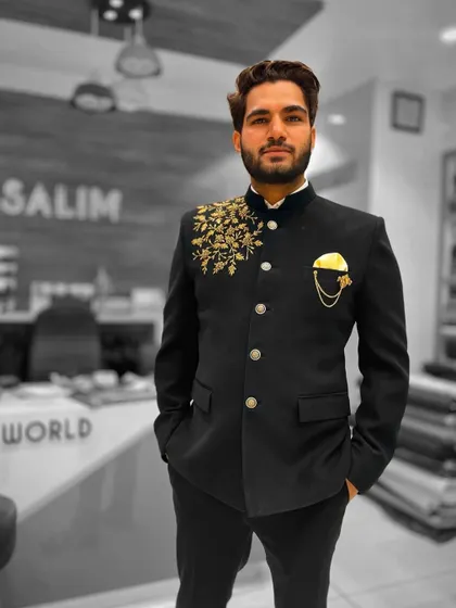 A client wearing a black Jodhpuri jacket with gold floral embroidery on one shoulder. The asymmetrical design is a modern twist on a classic silhouette.