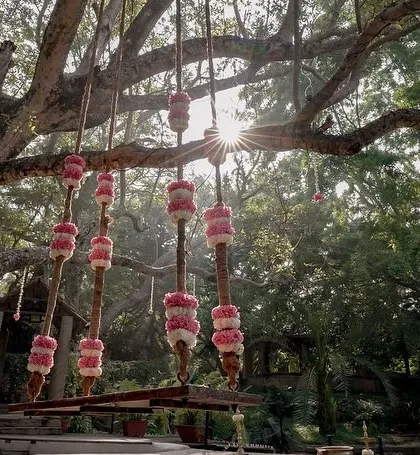 A swing decorated with pink floral elements, hanging from a large tree.