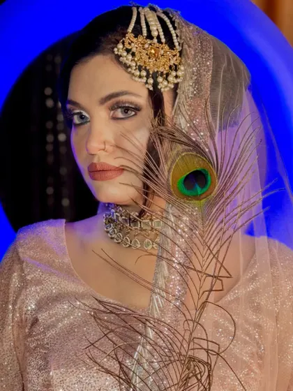 A dramatic and artistic shot. The model's intense gaze is complemented by the sharp winged liner and the creative placement of the peacock feather.