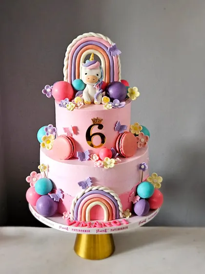 A magical unicorn and rainbow cake for a 6th birthday. This two-tier pink cake is decorated with macarons, colorful spheres, and a handmade unicorn topper.