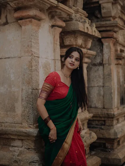 A model in a traditional saree stands against the stone pillars of a temple. The composition emphasizes the texture of both the ancient architecture and the classic Indian garment.