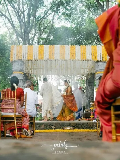 A candid moment from the guest's perspective, looking towards the beautifully decorated mandap. The vibrant colors of the guests' attire complement the traditional decor perfectly.