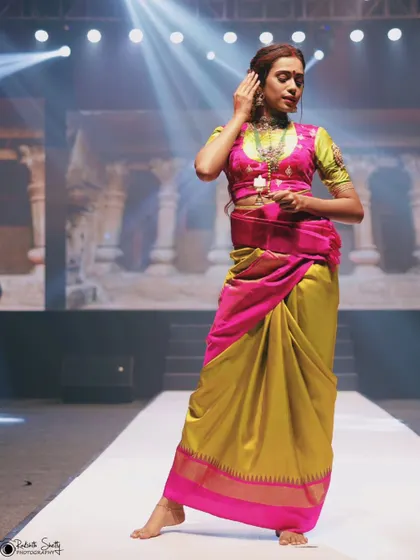 A full-body shot of the model in the vibrant pink and yellow-green saree. This image captures her complete look and confident pose against the backdrop of the fashion show's stage.
