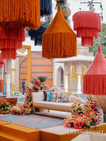 The bride's seating for the Soukh Bazaar Mehendi, framed by a cascade of colorful, oversized tassels and vibrant floral arrangements. This setup is a modern, elevated take on traditional Mehendi decor.