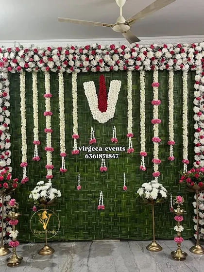 An elegant Ear Piercing ceremony backdrop made with a woven coconut leaf mat and decorated with floral garlands and a central 'Naamam' symbol.