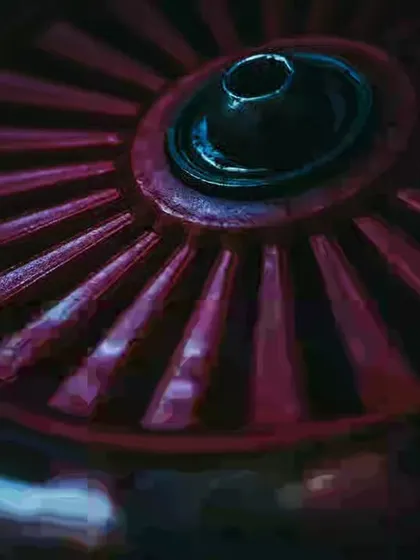 A close-up of a red industrial wheel. The dark, moody lighting and intense color create a powerful and abstract image from a mechanical object.