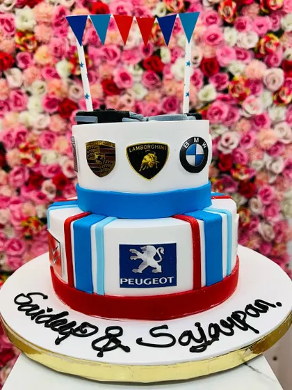 A two-tiered cake for a supercar fan, featuring logos of Porsche, Lamborghini, BMW, and Peugeot. A great way to celebrate a love for high-end cars.