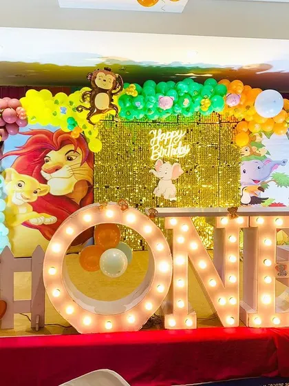 Another angle of a jungle-themed first birthday, showing the "ONE" marquee letters and a variety of animal props including a tall giraffe and a lion cub.