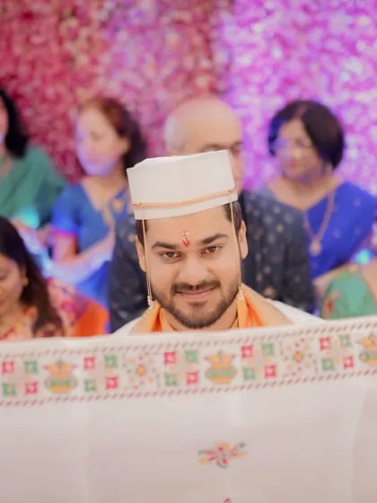 The groom peeks over the Antarpat, the traditional cloth that separates the couple, his smile full of anticipation before he sees his bride.