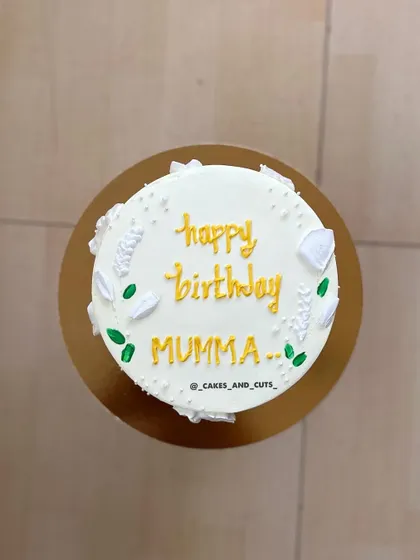 A top-down view of the "Happy Birthday Mumma" cake, showing the simple, heartfelt message and delicate piped leaves.