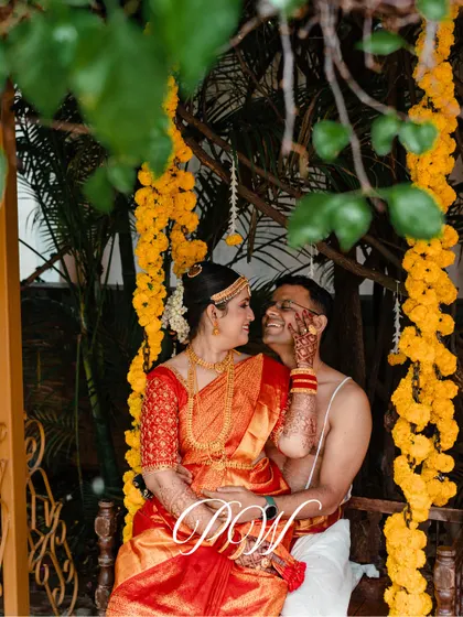 A happy couple sharing a moment on the traditional wedding swing (Oonjal), decorated with bright yellow marigolds. These candid shots are what make a wedding album truly special.