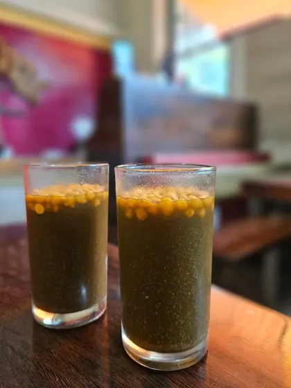 Two glasses of our refreshing, house-made Jaljeera Pani. It's the perfect drink to cleanse your palate and aid digestion after a hearty meal.