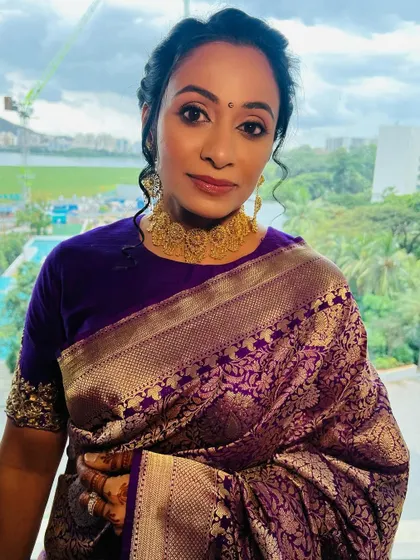 A portrait showcasing the soft glam makeup against her beautiful purple and gold saree. The look is elegant, radiant, and perfect for a South Indian wedding.
