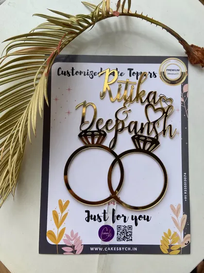 The "Ritika & Deepansh" engagement topper, shown here in its packaging, ready to add a personalized touch to their celebration.