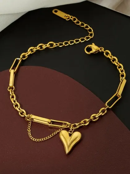 The trendy paperclip chain bracelet with a heart charm, displayed on a rich, dark background to highlight its gold tone.
