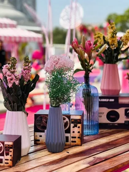 A close-up of a table centerpiece at a carnival-themed party, featuring flowers in quirky vases styled to look like old-school tape recorders.