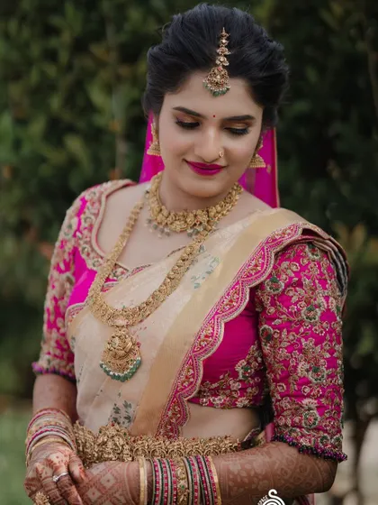 A bride in a cream and pink Kanchipuram saree with a heavily embroidered pink blouse. The floral motifs on the blouse are a beautiful example of our detailed handwork.