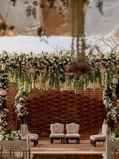 An elegant mandap with white floral arrangements against a rustic brick wall. This blend of classic and contemporary decor makes for beautiful wedding photos.