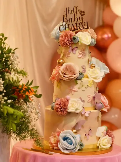 An elegant 8 kg, three-tier, no-fondant cake for a baby's meet and greet party. The design features delicate sugar flowers and butterflies, creating a whimsical and sophisticated centerpiece.
