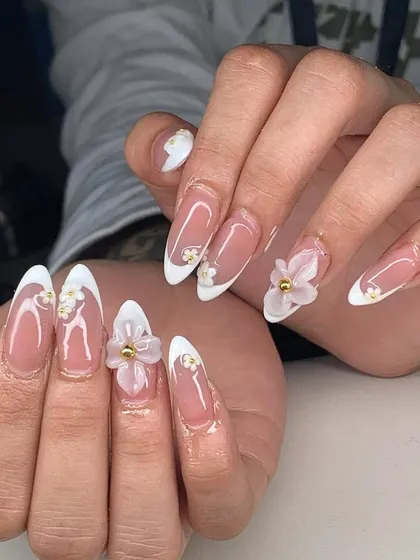 A beautiful example of 3D floral art on long stiletto nails. The classic French tips are elevated with delicate white flowers and gold bead centers.