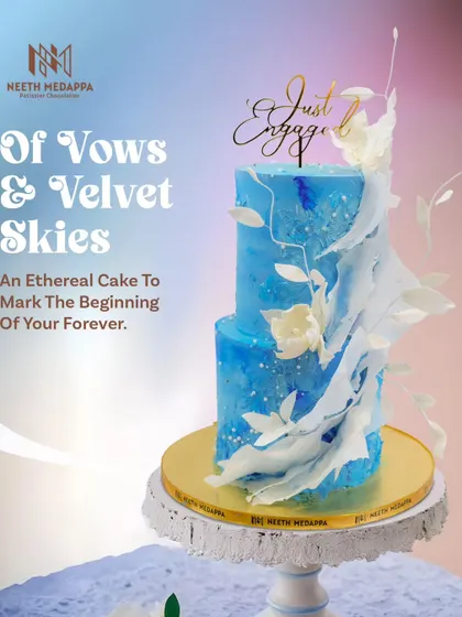 An ethereal cake to mark the beginning of your forever. This two-tiered engagement cake in shades of velvet sky blue is adorned with delicate, cascading sugar art and white florals.