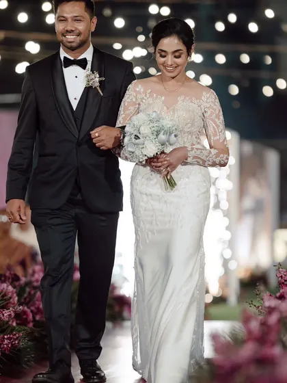 The couple makes their way down the aisle for their reception. The path is lined with soft florals and illuminated by string lights and sparklers, creating a warm and welcoming entrance.