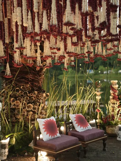 An evening shot of the couple's seating, where the warm lighting enhances the rich textures of the floral hangings and bell pillars.