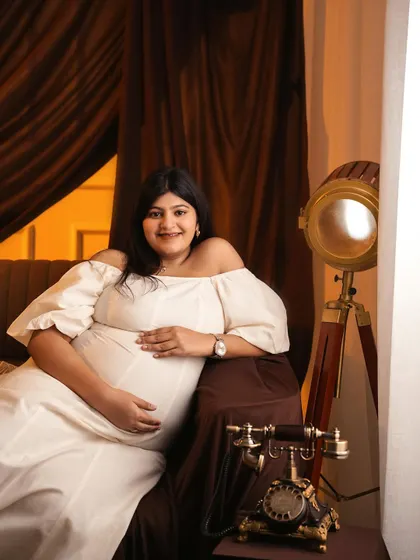 A relaxed seated portrait in the same vintage-themed setup, showing a different perspective and pose option for your studio maternity shoot.