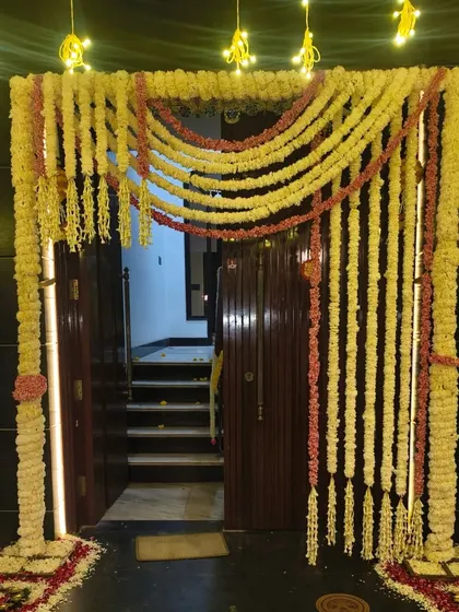 A traditional and elaborate floral entrance decoration for a home Diwali puja. The entire door frame is covered in garlands of white and pink flowers, with flower petal rangoli at the base.